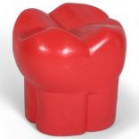 A red plastic stool in the form of a molar or tooth, possibly from a dentist’s waiting room, with