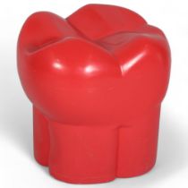 A red plastic stool in the form of a molar or tooth, possibly from a dentist’s waiting room, with