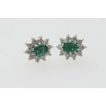 Pair of emerald and diamond cluster earrings, the central oval cut emerald of approx. 0.5ct,