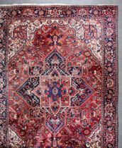 An Early 20th Century Heriz Carpet, woven in colours of ivory, navy blue, and wine, with a central