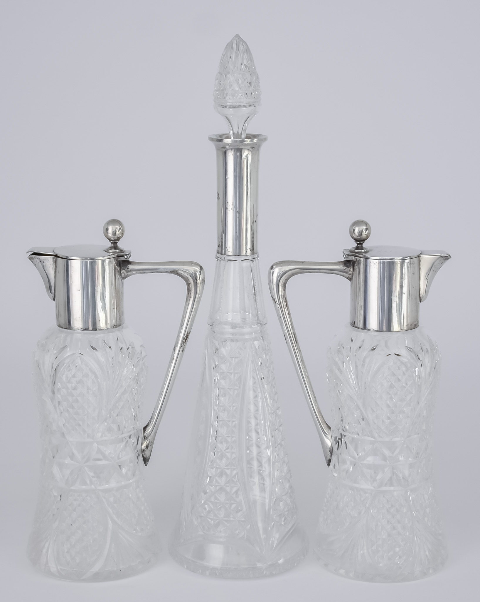 A Pair of German Silver Mounted and Cut Glass Claret Jugs and a Similar Decanter, the claret jugs