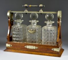 An Edwardian Oak and Plated Metal Mounted Three Bottle Spirit Tantalus, containing three hobnail cut