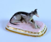 CHAMBERLAIN’S WORCESTER PORCELAIN MODEL OF A RECUMBENT GREYHOUND, painted in colours, on a pink