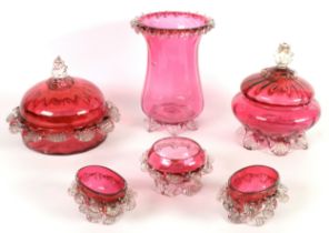 TWO CRANBERRY GLASS CIRCULAR JARS AND COVERS, one with moulded clear glass feet, the other with