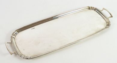 GEORGE V PLAIN SILVER TWO HANDLED TRAY, of narrow oblong form with shaped corners to the moulded