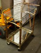 A GOLD COLOURED AND GLASS TWO TIER TEA TROLLEY