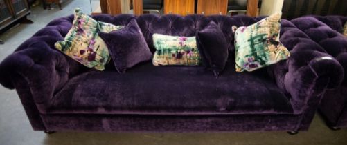 A STYLISH FULLY UPHOLSTERED PURPLE VELVET COVERED THREE SEATER CHESTERFIELD SETTEE, RAISED ON TURNED
