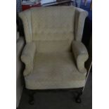 A WINGED FIRESIDE ARMCHAIR, COVERED IN BEIGE FABRIC AND RAISED ON CLAW AND BALL LEGS