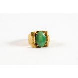 CHINESE GOLD RING set with an oval green jade in an Art Deco cup setting, broad shank, 8.8gms gross,