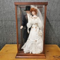 A Franklin Mint porcelain bride and groom doll in a perspex case, case 64 x 34 x 34cm.