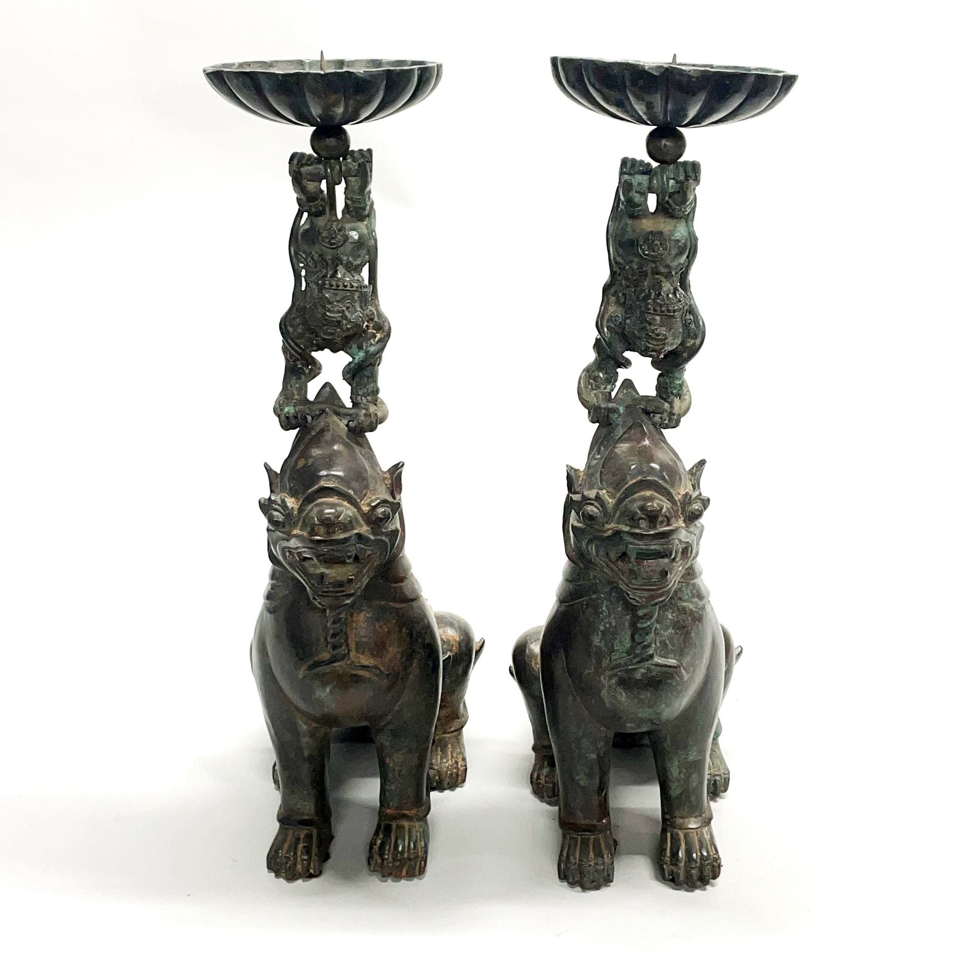A pair of large Chinese bronze mythical animal pricket candlesticks featuring liondogs performing