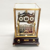 A brass and glass cased Congreave style clock mounted on a wooden base, 39.5 x 23 x 23cm.