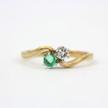An 18ct yellow gold emerald and diamond set crossover ring, (L.5).