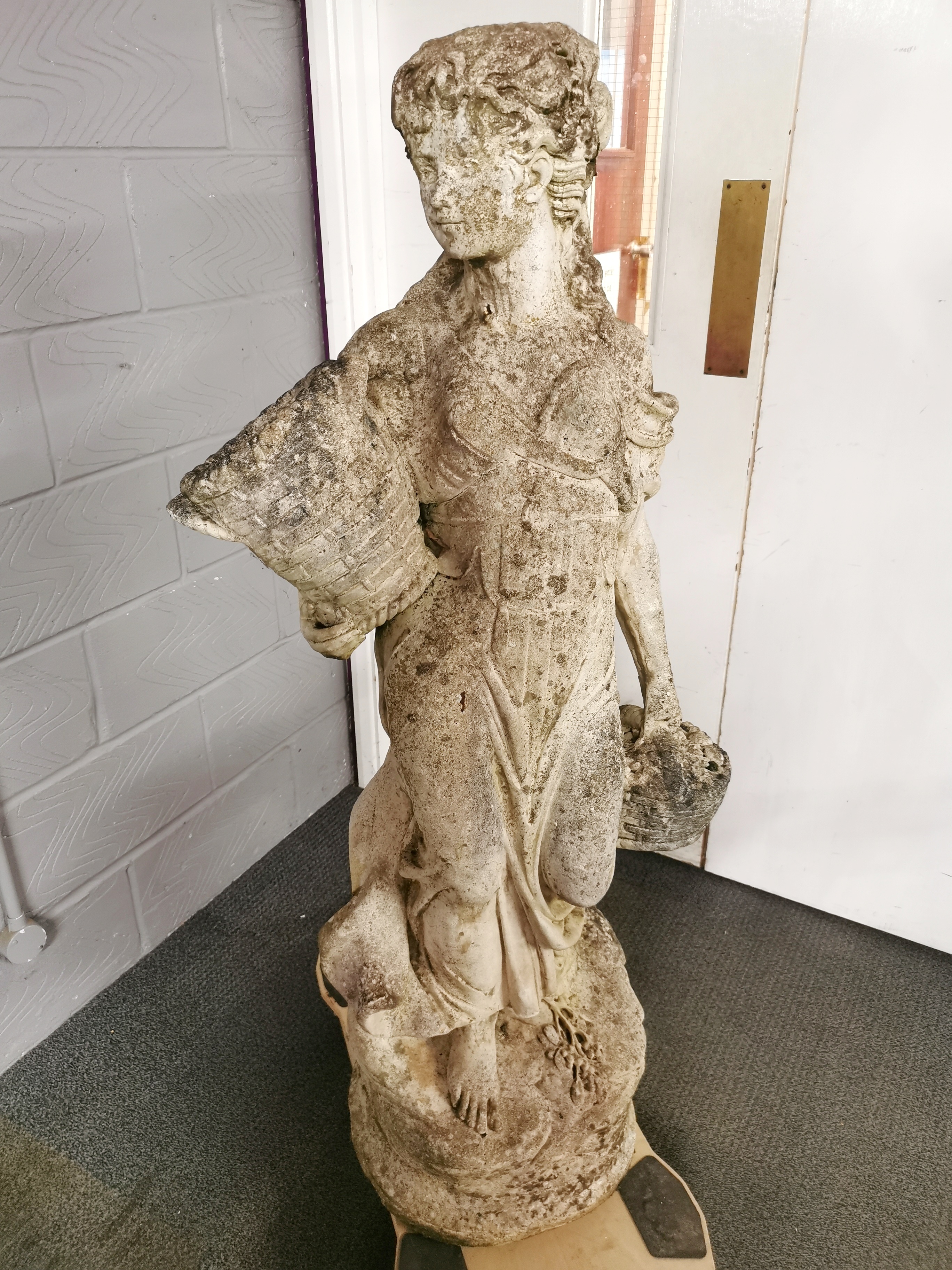 A large antique carved stone garden figure of a woman carrying baskets, H. 136cm base W. 40cm.