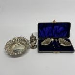 A cased pair of white metal salts with hallmarked silver spoons and embossed white metal dish and