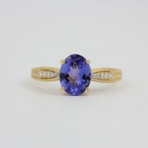 An 18ct yellow gold ring set with an oval cut tanzanite and diamond set shoulders, (Q).