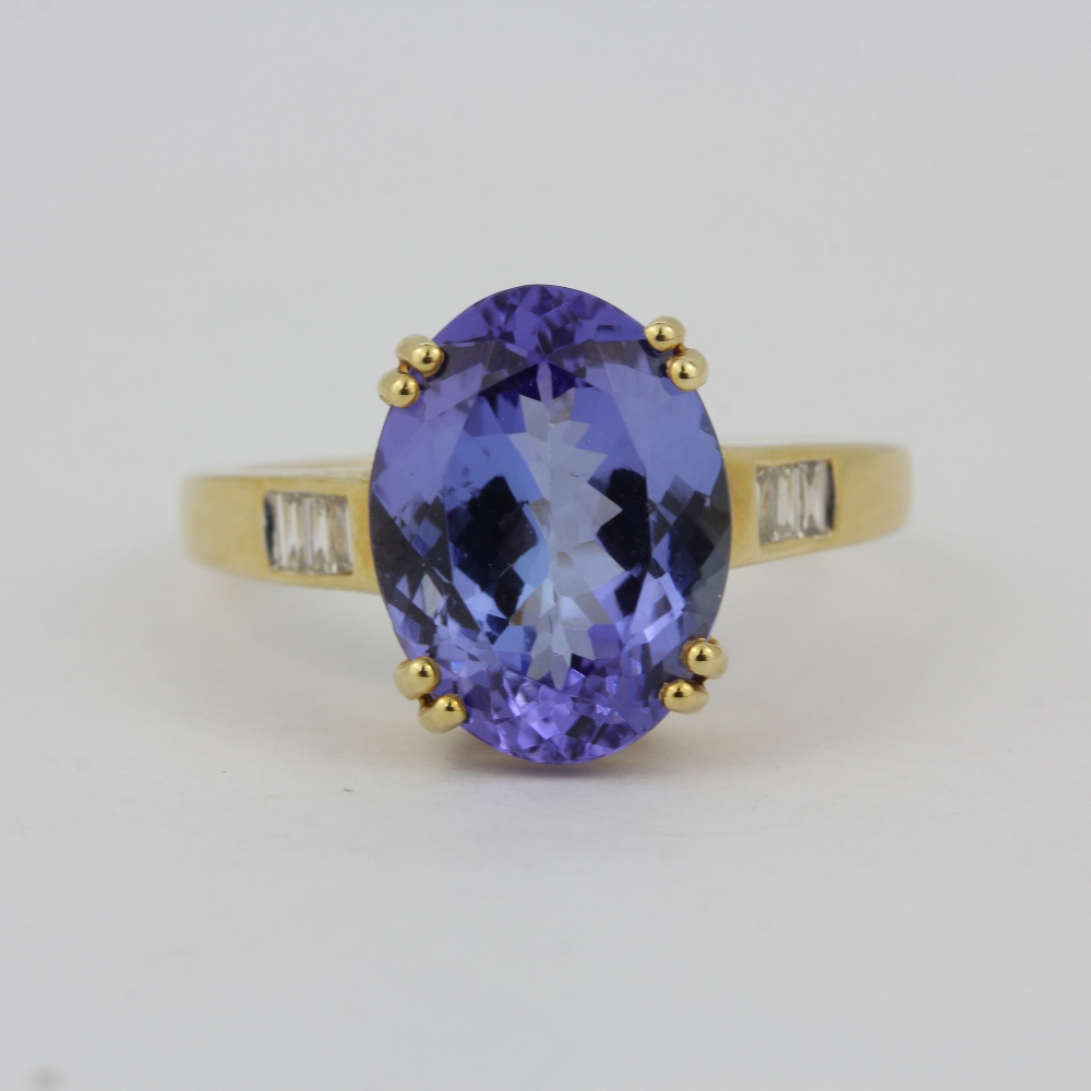 A hallmarked 14ct yellow gold ring set with a large oval cut tanzanite and baguette cut diamond