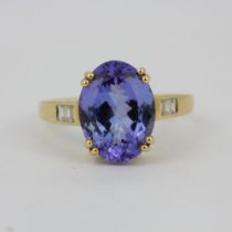 A hallmarked 14ct yellow gold ring set with a large oval cut tanzanite and baguette cut diamond
