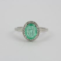 A hallmarked 14ct white gold ring set with an oval cut emerald surrounded by diamonds, (O).