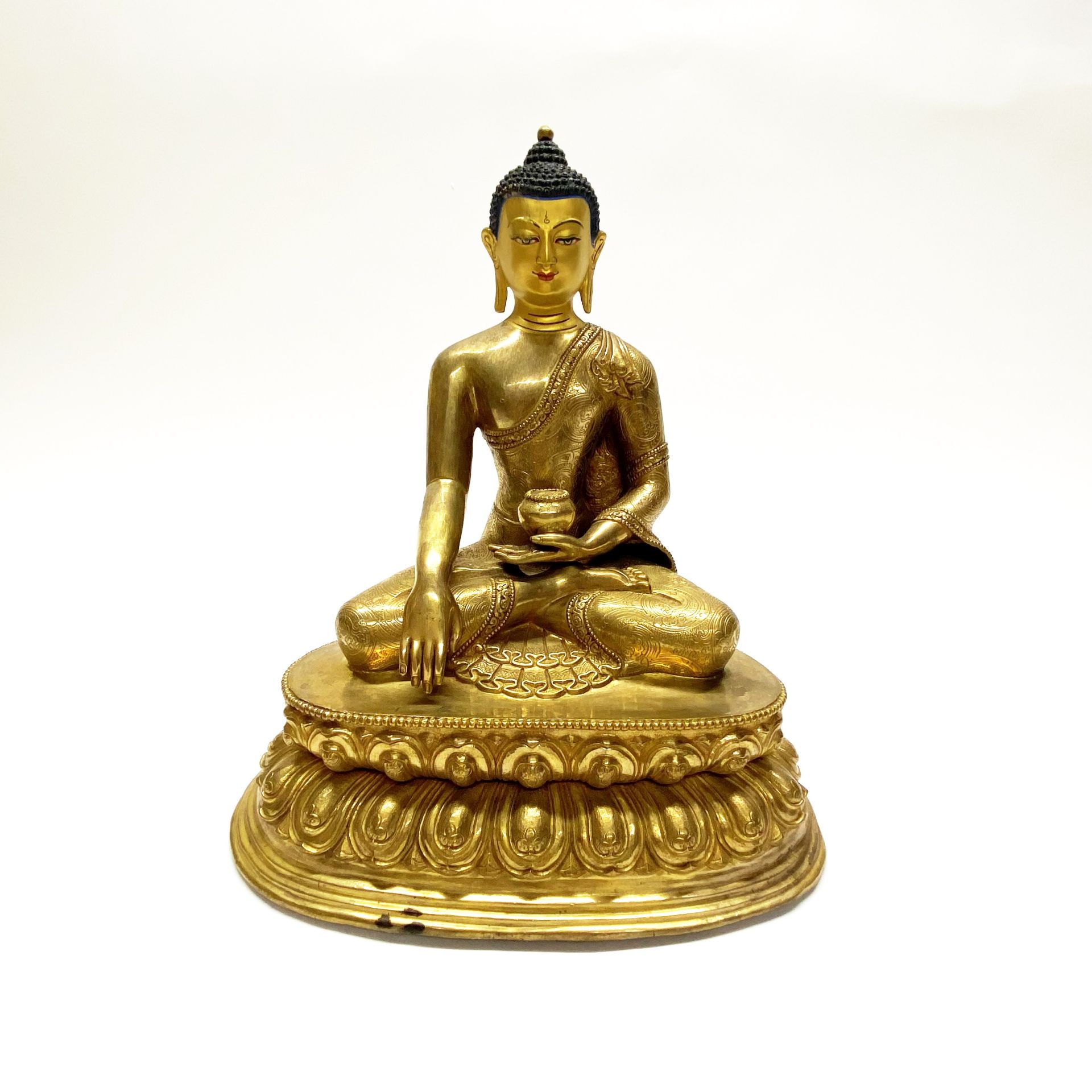 A Tibetan gilt bronze figure of seated Buddha with hand painted temple quality face. H. 30cm