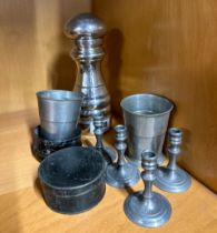 A large pepper grinder with three folding beakers and four pewter candlesticks.
