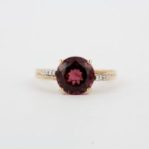 A 14ct rose gold ring set with a round cut garnet and diamond set shoulders, (O).