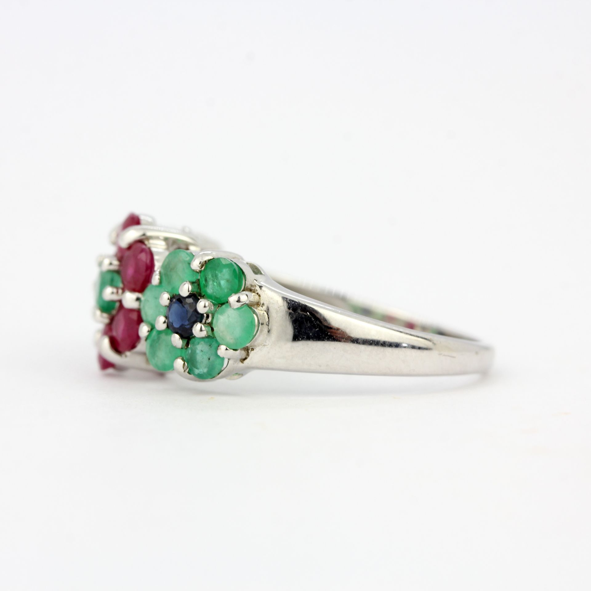 A 9ct white gold flower shaped triple cluster ring set with rubies, emeralds and sapphires, (O). - Image 2 of 3