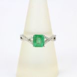 An 18ct white gold ring set with an emerald cut emerald and diamond set shoulders, ring size O.5.