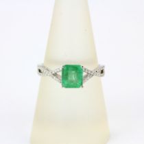 An 18ct white gold ring set with an emerald cut emerald and diamond set shoulders, ring size O.5.