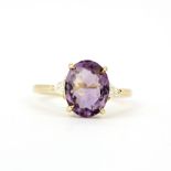 A 9ct yellow gold ring set with an oval cut amethyst flanked by trillion cut diamonds, ring size O.