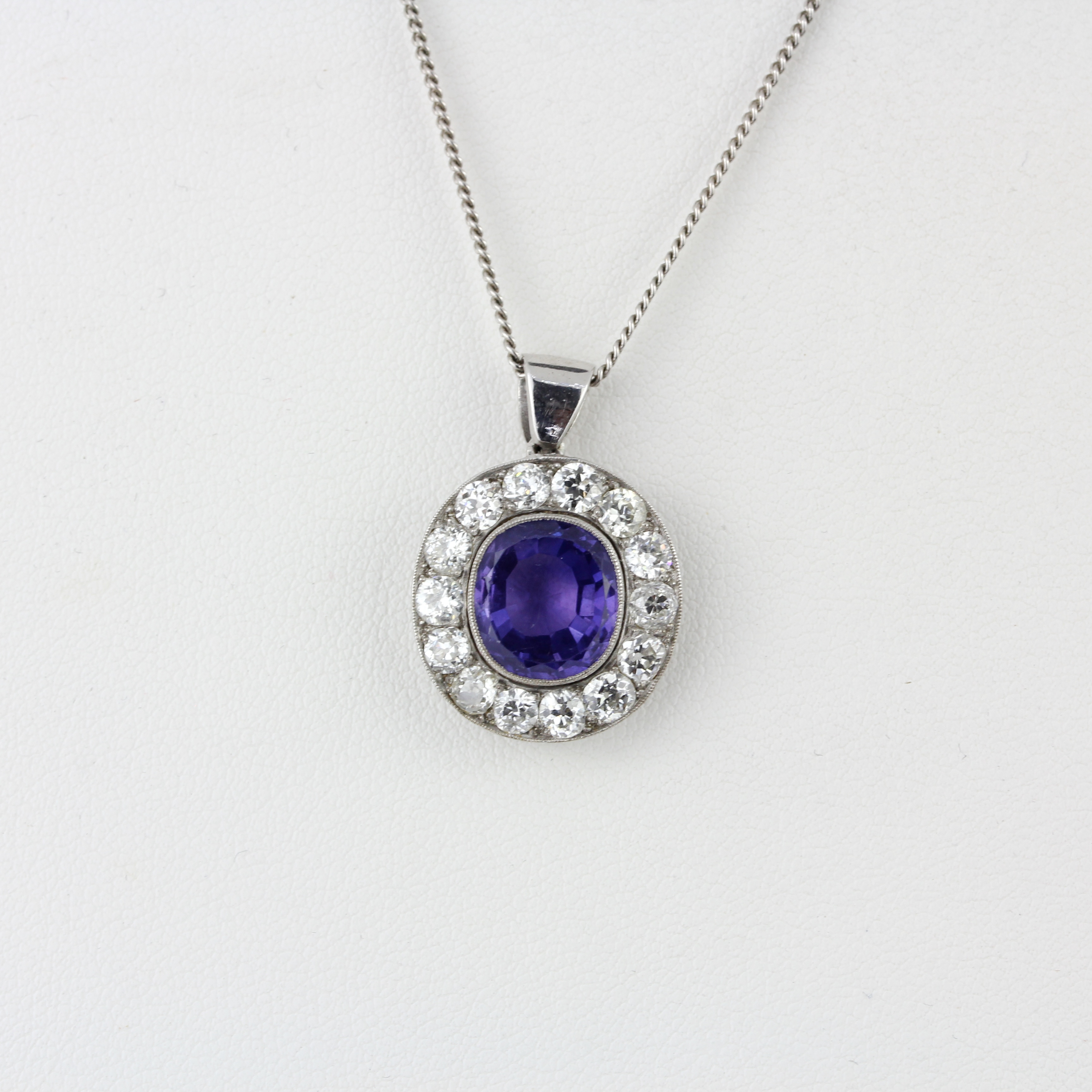 A white metal (tested minimum 9ct gold) pendant set with an oval cut purplish sapphire surrounded by