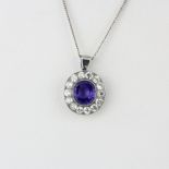 A white metal (tested minimum 9ct gold) pendant set with an oval cut purplish sapphire surrounded by