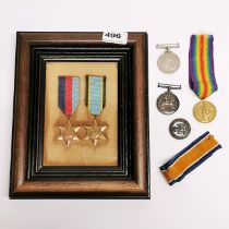 A frame containing two WWII medals with three others and a badge.