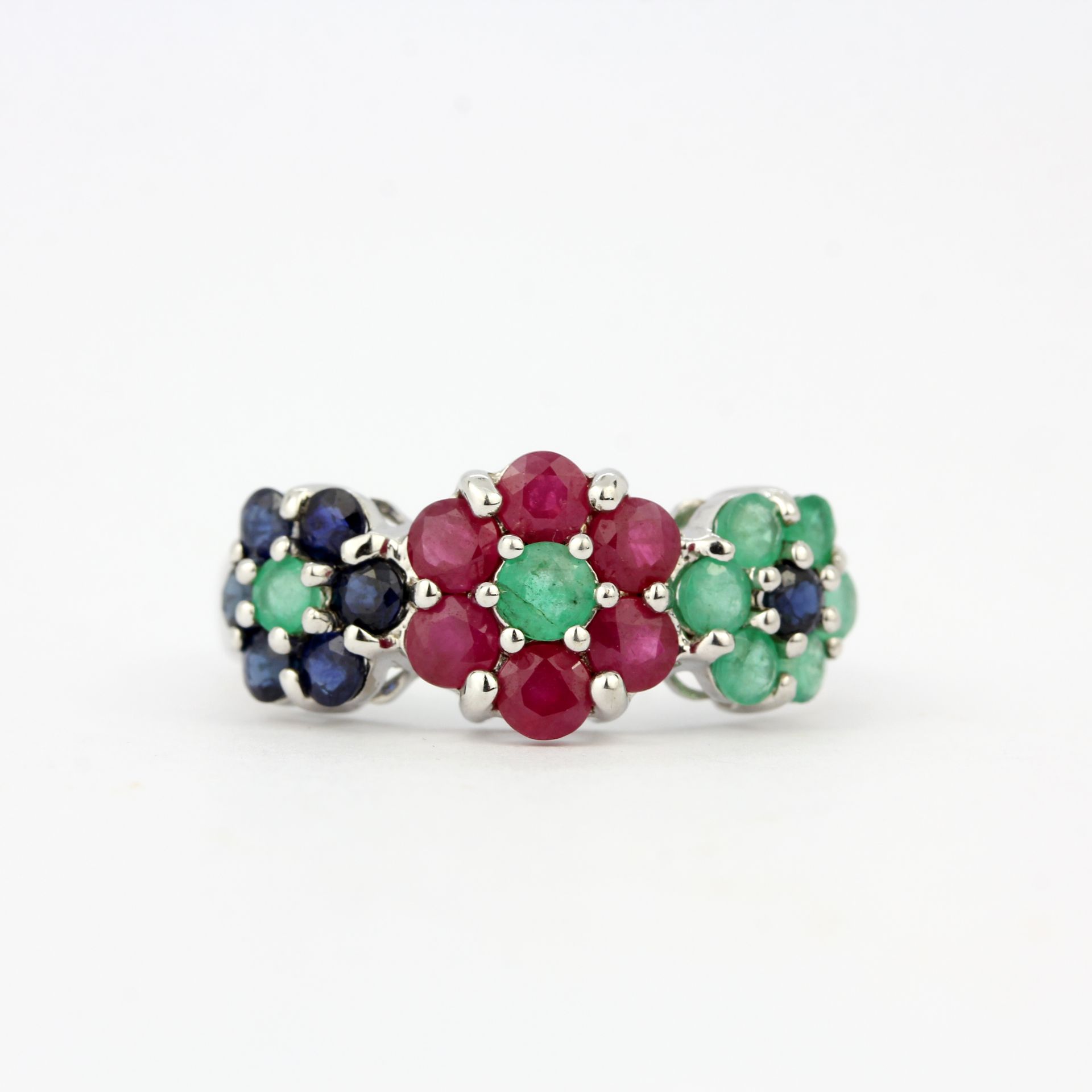 A 9ct white gold flower shaped triple cluster ring set with rubies, emeralds and sapphires, (O).