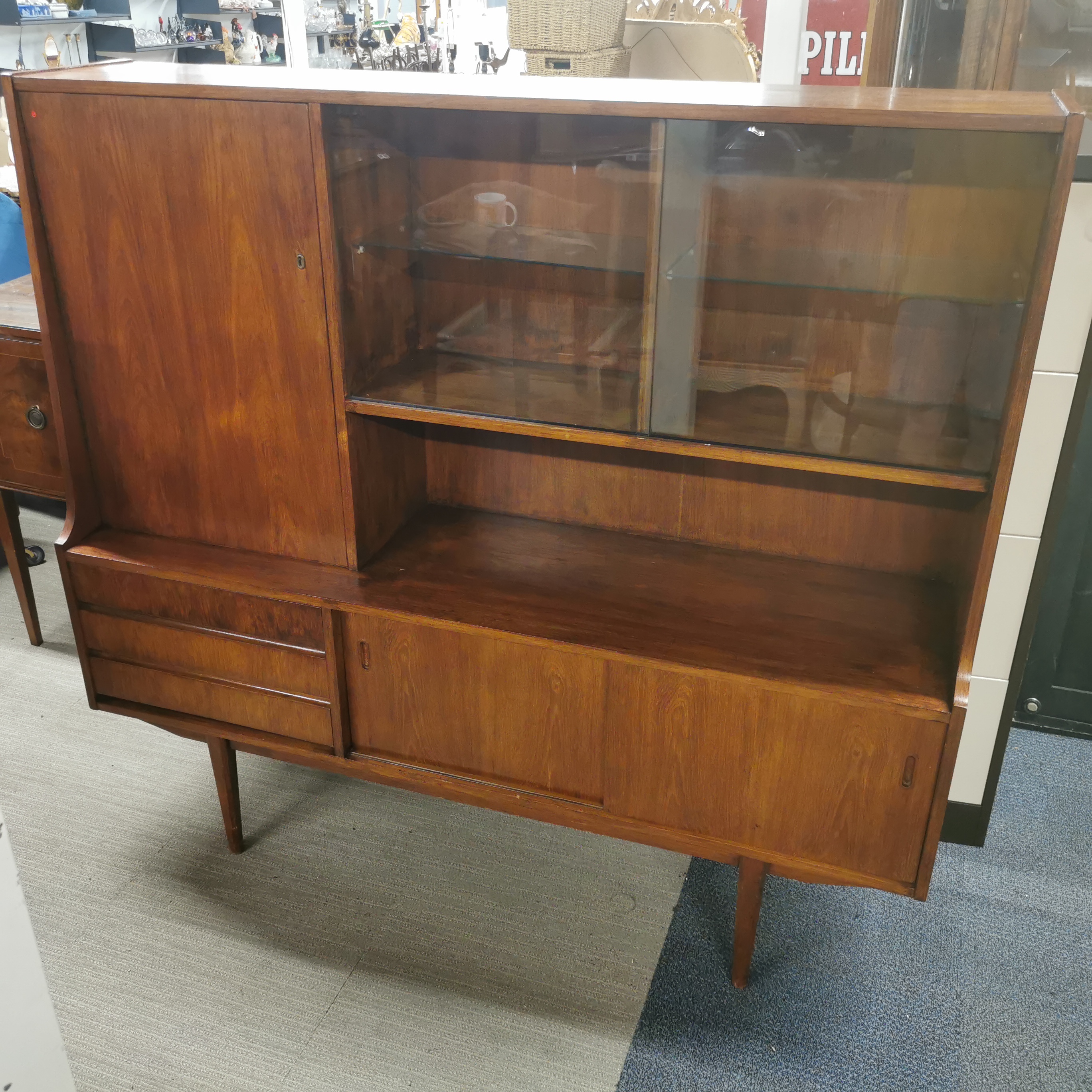 A mid 20thC teak three drawer cabinet with glass shelves and sliding doors, 152.5 x 141 x 40cm.