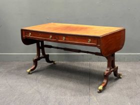 A late Regency mahogany sofa table on shaped end supports, down swept legs and brass paw caps, 69