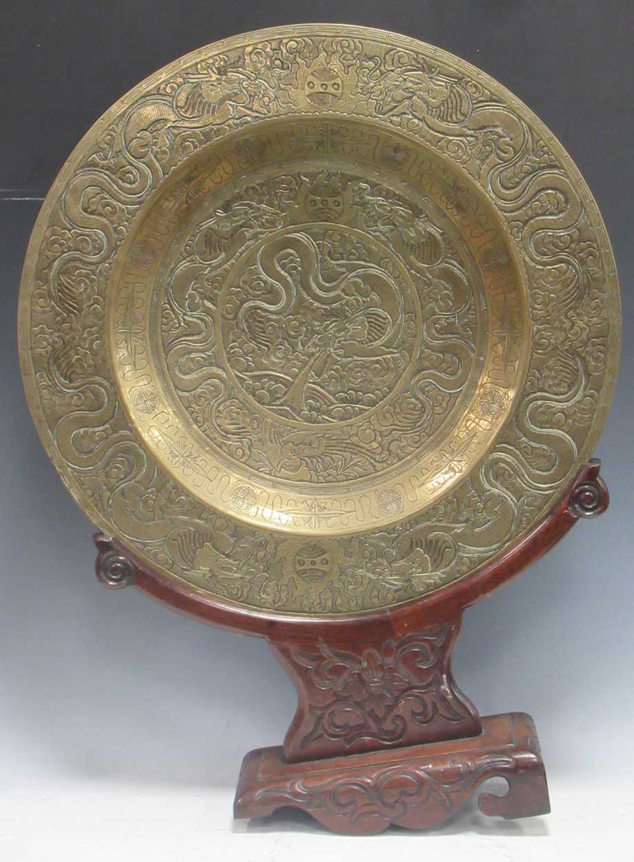 A Chinese circular brass dish on carved wood stand, early 20th century, decorated in relief with