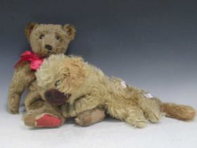 A old teddy bear, probably 1920s, with long snout, some wear and tear, and a blond plush dog