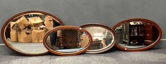 Four oval wall mirrors, to include two Edwardian inlaid mahogany mirrors 46 x 74cm and 53 x 84cm; an