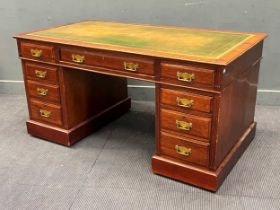 An Edwardian mahogany pedestal desk, with inset green faux leather top over an assortment of nine