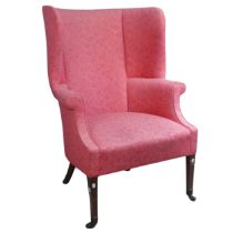 An antique wing-back Armchair, upholstered in pink, raised on tapering front legs with castors and