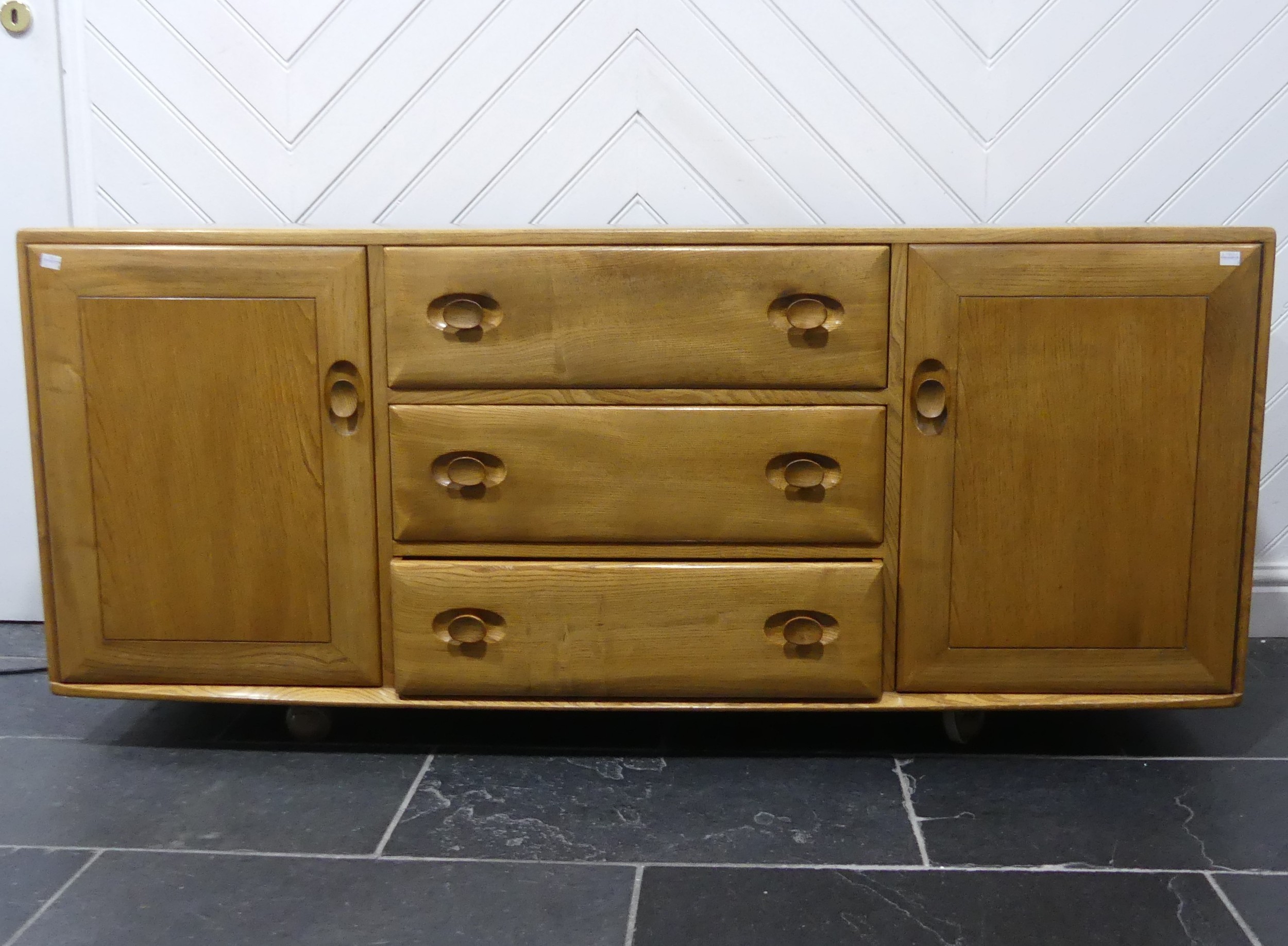 An Ercol "Windsor" blond elm Sideboard, model No. 455, fitted with three central drawers with an