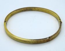 A hinged yellow metal bangle, tests electronically