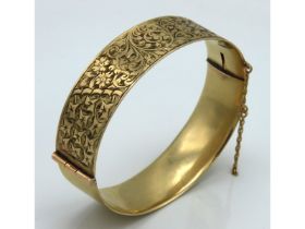 A 9ct gold solid metal core bangle with chased flo