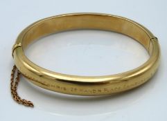 A hinged yellow metal bangle, tests electronically