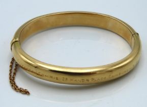 A hinged yellow metal bangle, tests electronically