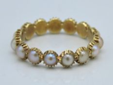 A yellow metal eternity ring set with pearl, tests