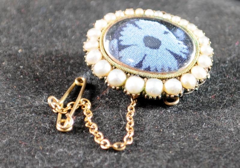 19th C pinchbeck mourning brooch with seed pearls set around an embroidered flower.