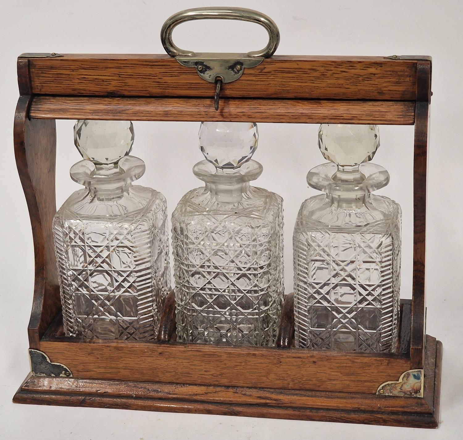 Vintage oak tantulus containing a matching set of three crystal glass decanters. Includes key.