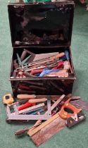 Black tin box containing a large collection of vintage hand tools.